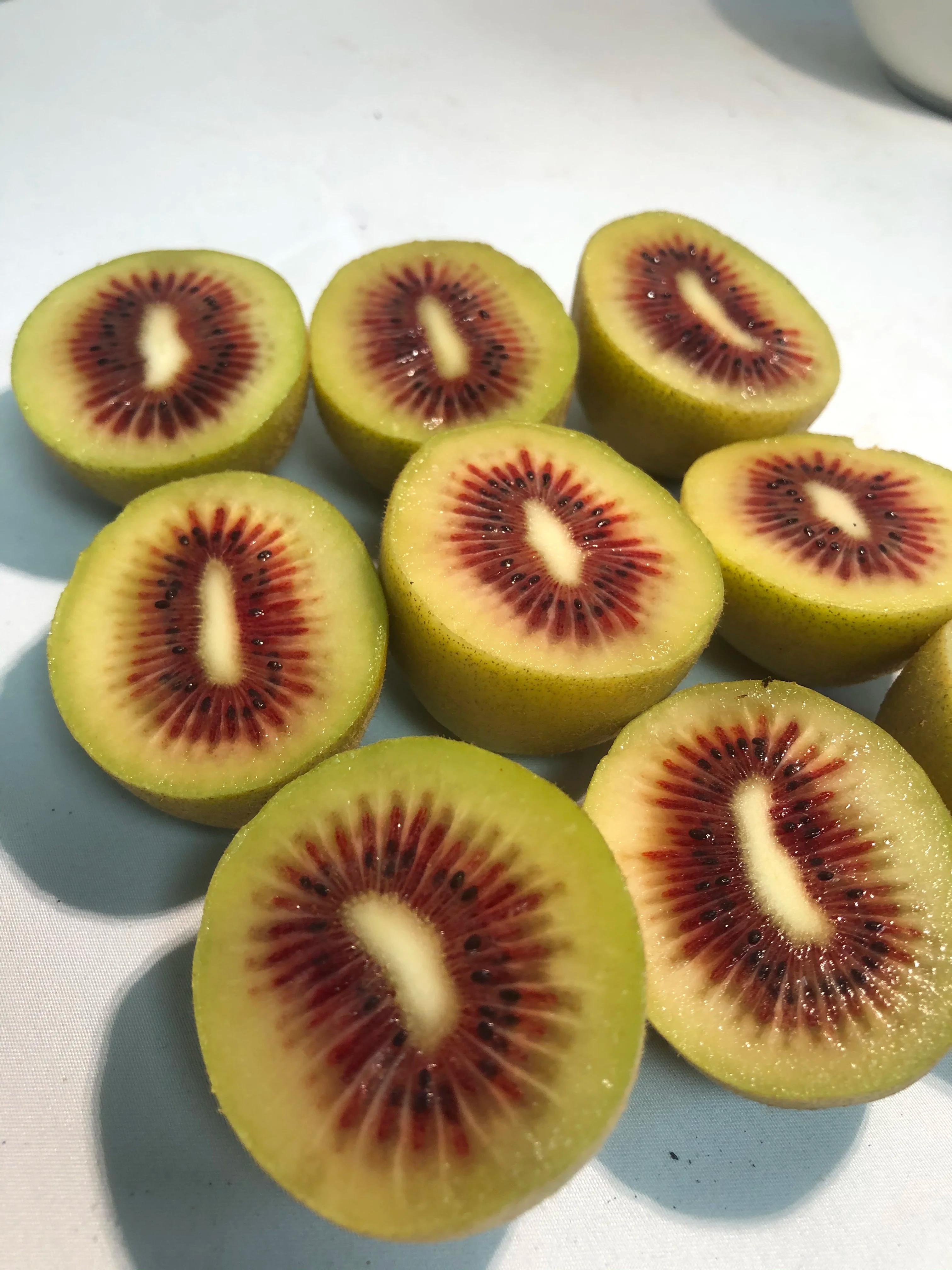 Tranches de kiwis avec des graines rouges sur une surface blanche.